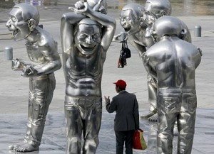 Esculturas de Yue Minjun situadas en los exteriores del Museo de Arte Contemporáneo de Pekín, un viandante circula entre ellas. Se observa como las figuras tienen, aproximadamente, el doble de la escala humana.